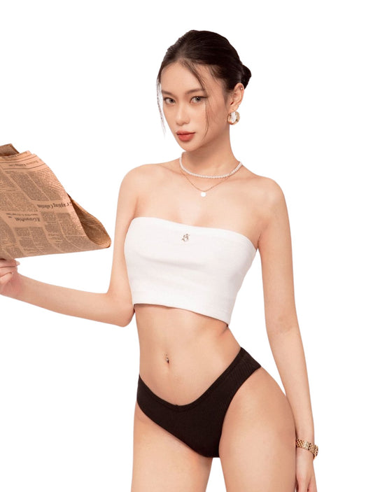 Woman wearing a white strapless top and black high-waisted bikini bottom, holding a newspaper.