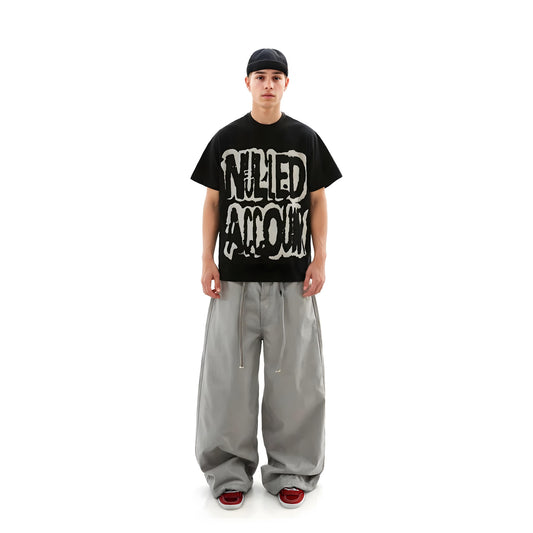 Person wearing a black t-shirt with graphic design and gray pants on a white background