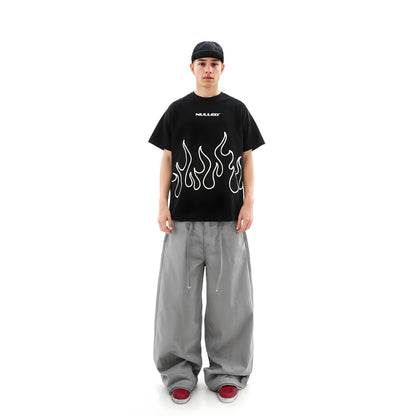 Person wearing a black t-shirt with flame design and gray pants on a white background