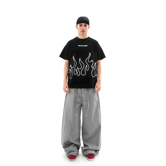 Person wearing a black t-shirt with flame design and gray pants on a white background