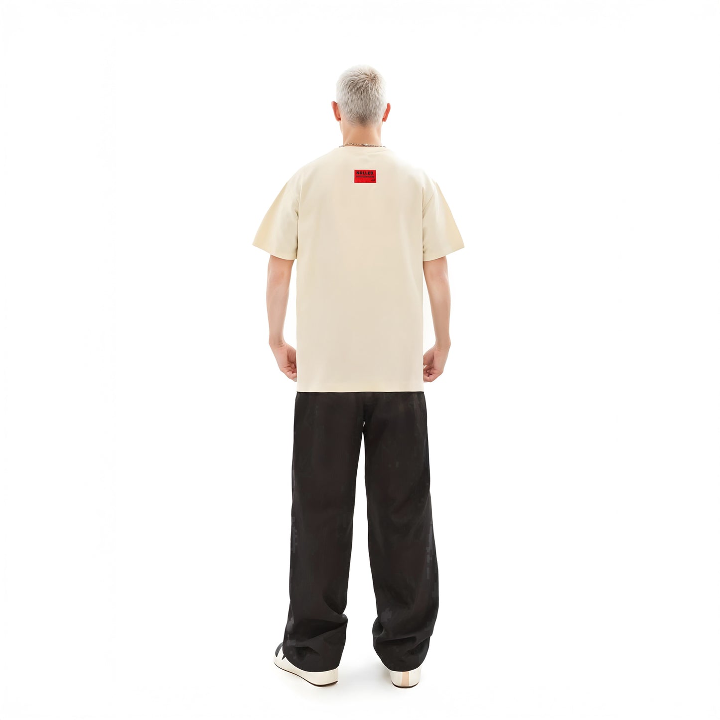 Person wearing a beige t-shirt with a red logo on the back, standing against a white background
