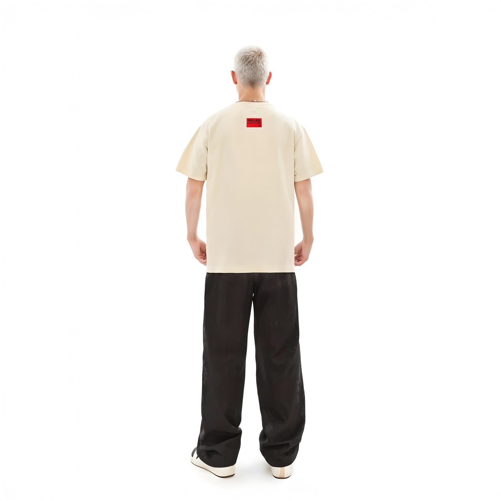 Person wearing a beige t-shirt with a red logo on the back, standing against a white background