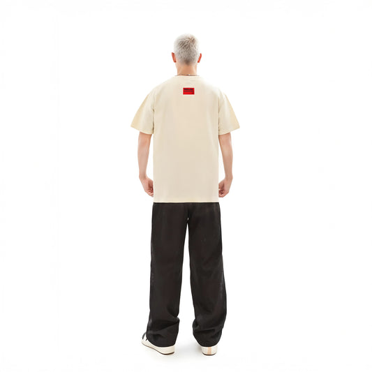 Person wearing a beige t-shirt with a red logo on the back, standing against a white background