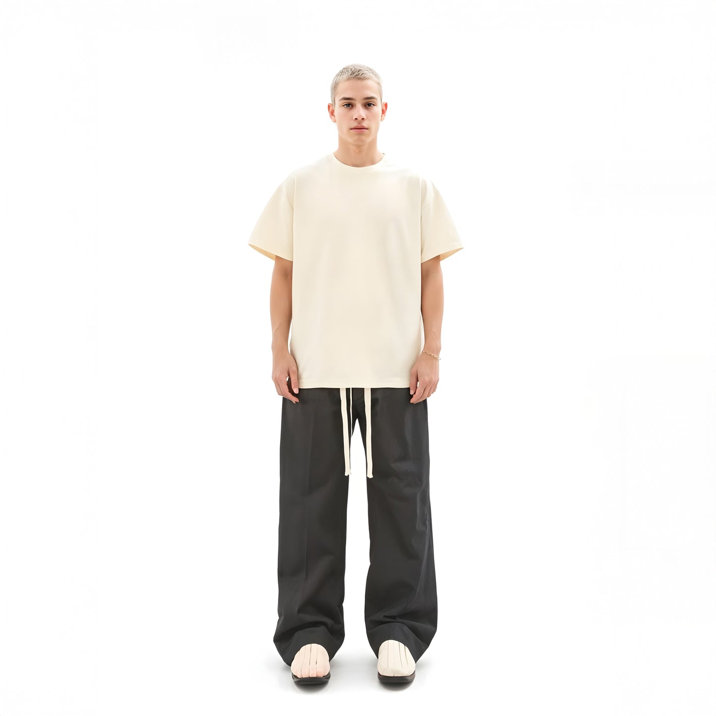 Person wearing a beige oversized t-shirt and black pants on a white background