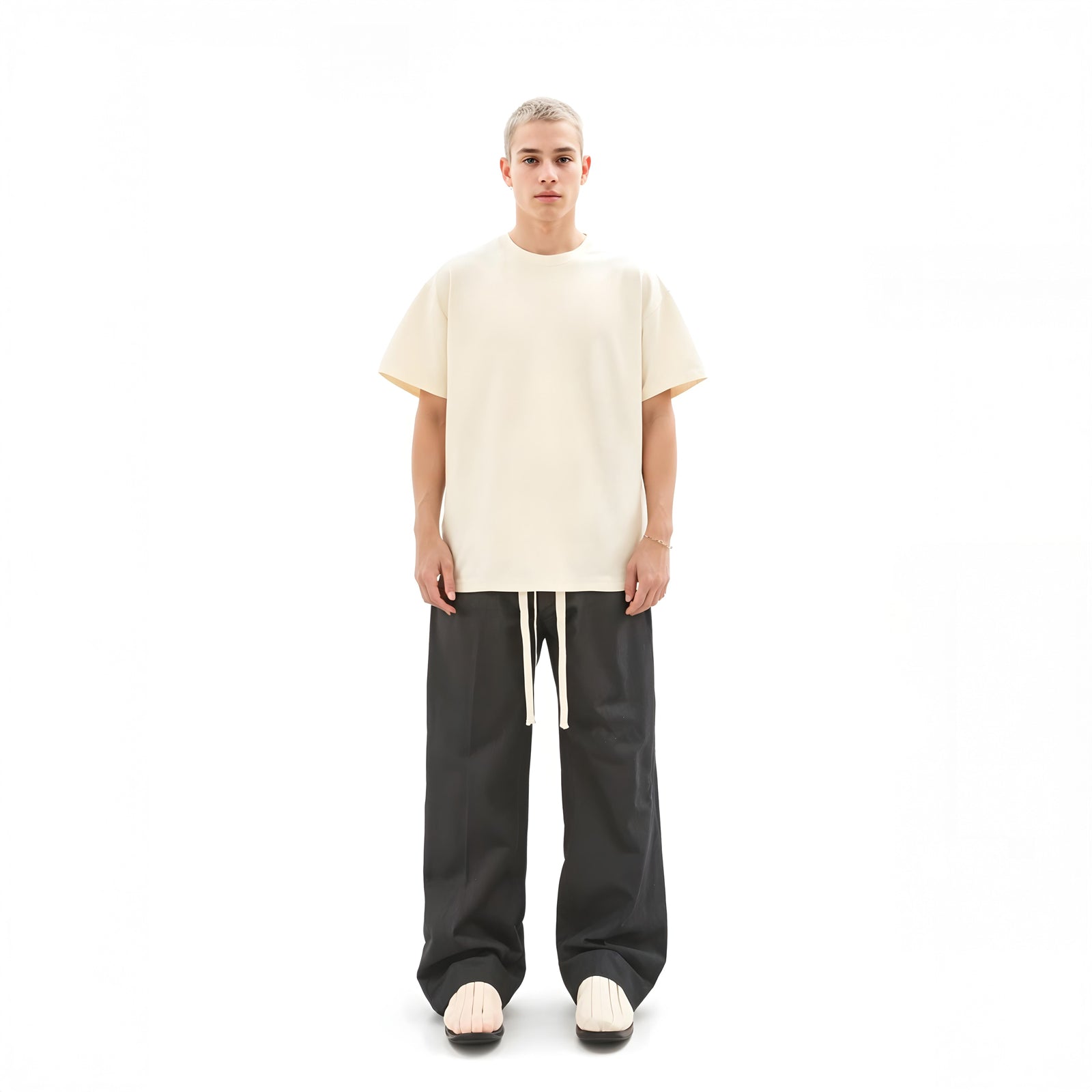 Person wearing a beige oversized t-shirt and black pants on a white background