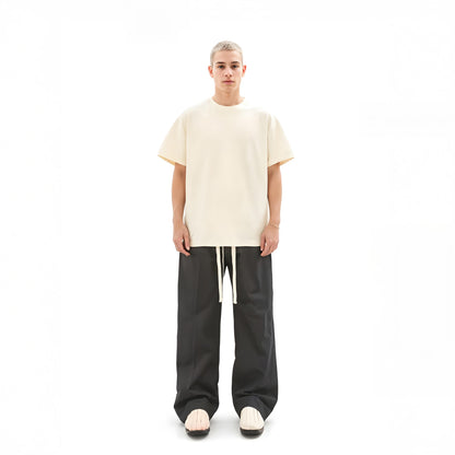 Person wearing a beige oversized t-shirt and black pants on a white background