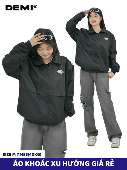 Two people wearing black jackets and gray pants with sunglasses, standing against a white background. DEMI brand is visible.