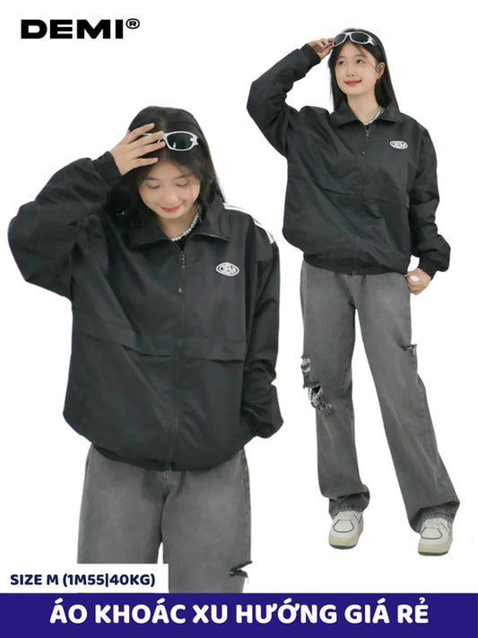 Two people wearing black jackets and gray pants with sunglasses, standing against a white background. DEMI brand is visible.