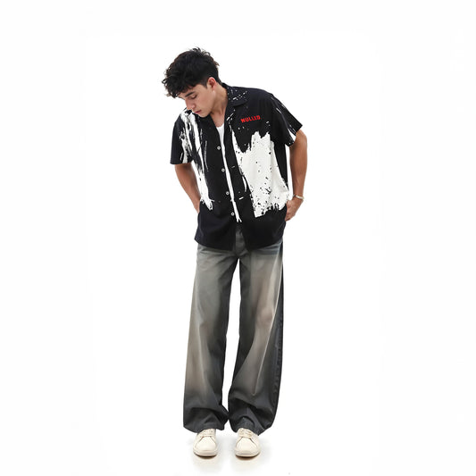 Person wearing a black and white patterned shirt with text, gray pants, and white shoes on a white background