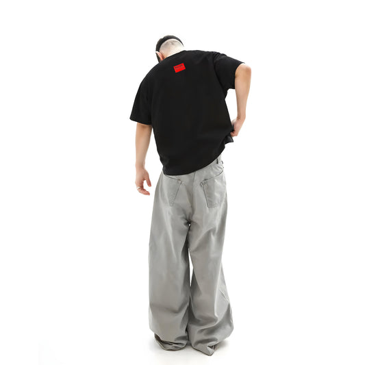Person wearing a black t-shirt with a red label and gray pants on a white background