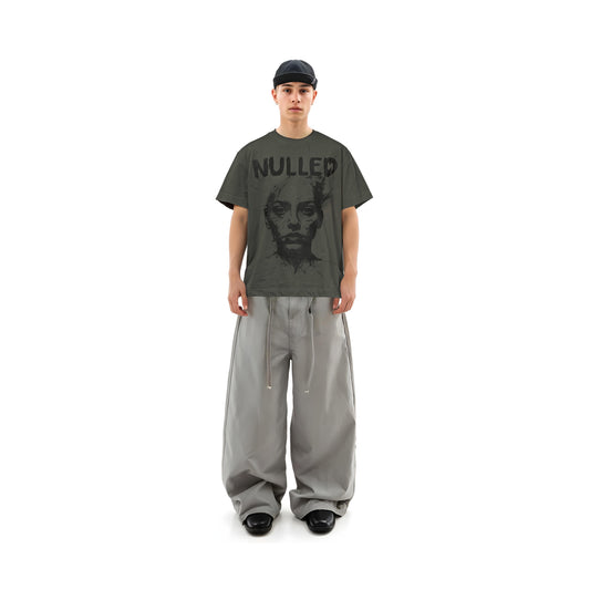 Person wearing a dark gray t-shirt with 'NULLED' text and a graphic design, paired with light gray pants on a white background.