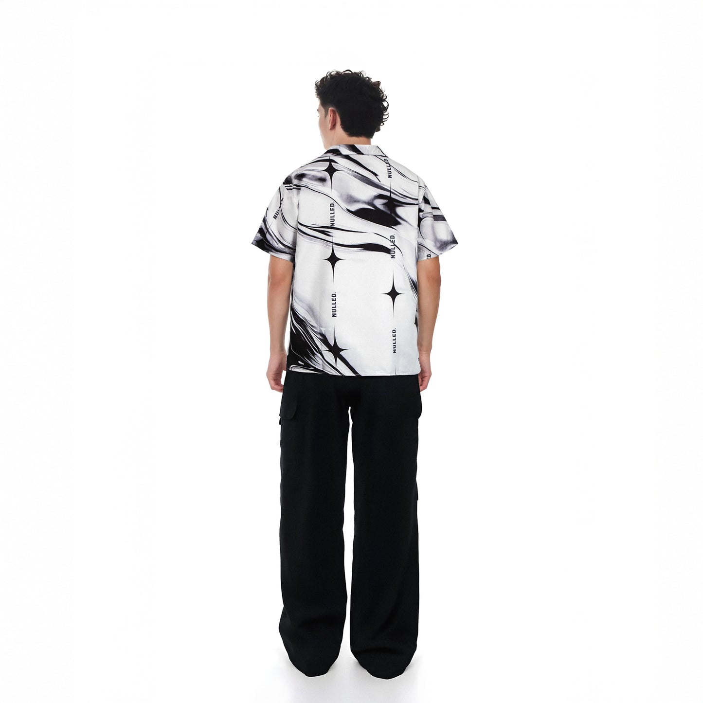 Person wearing a black and white patterned shirt with black pants on a white background