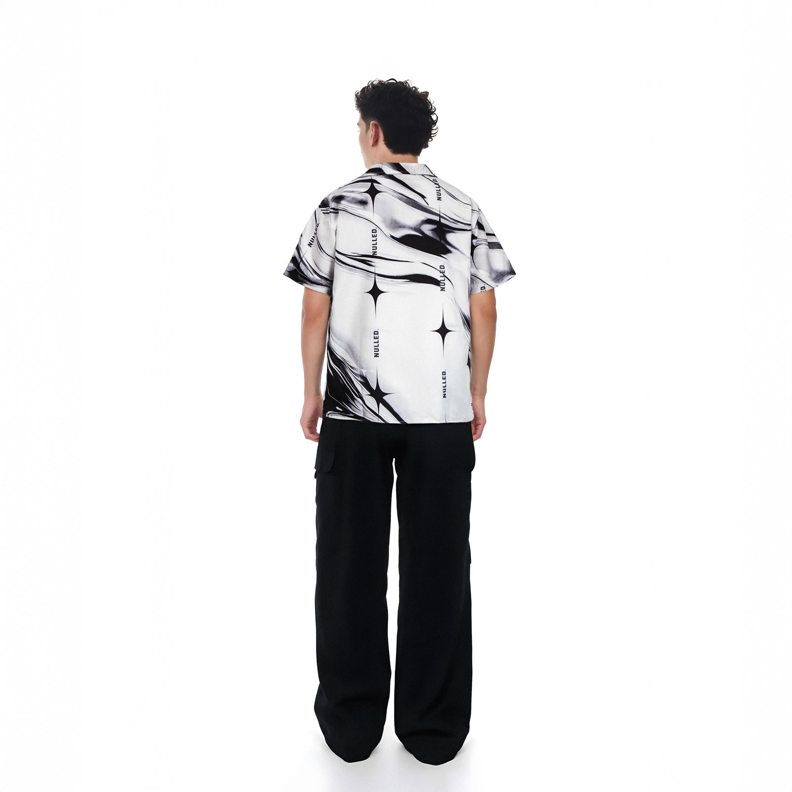 Person wearing a black and white patterned shirt with black pants on a white background