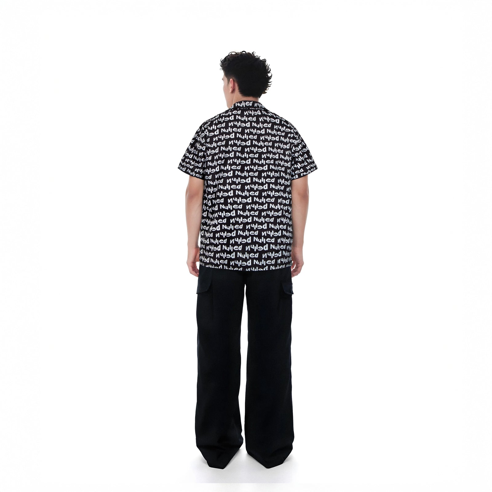 Person wearing a black and white patterned shirt with wide-leg pants on a white background