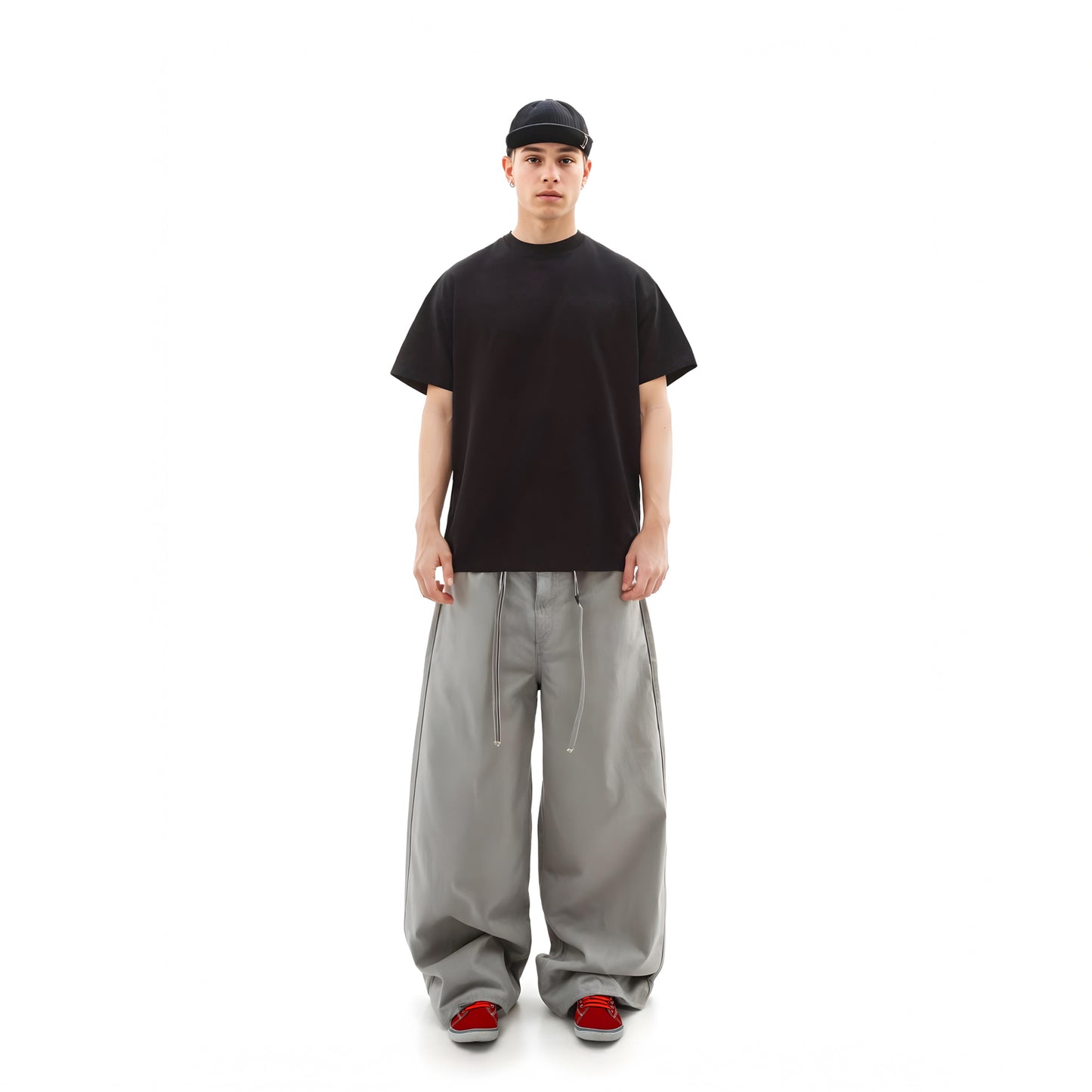 Person wearing a black t-shirt, gray pants, and red shoes on a white background
