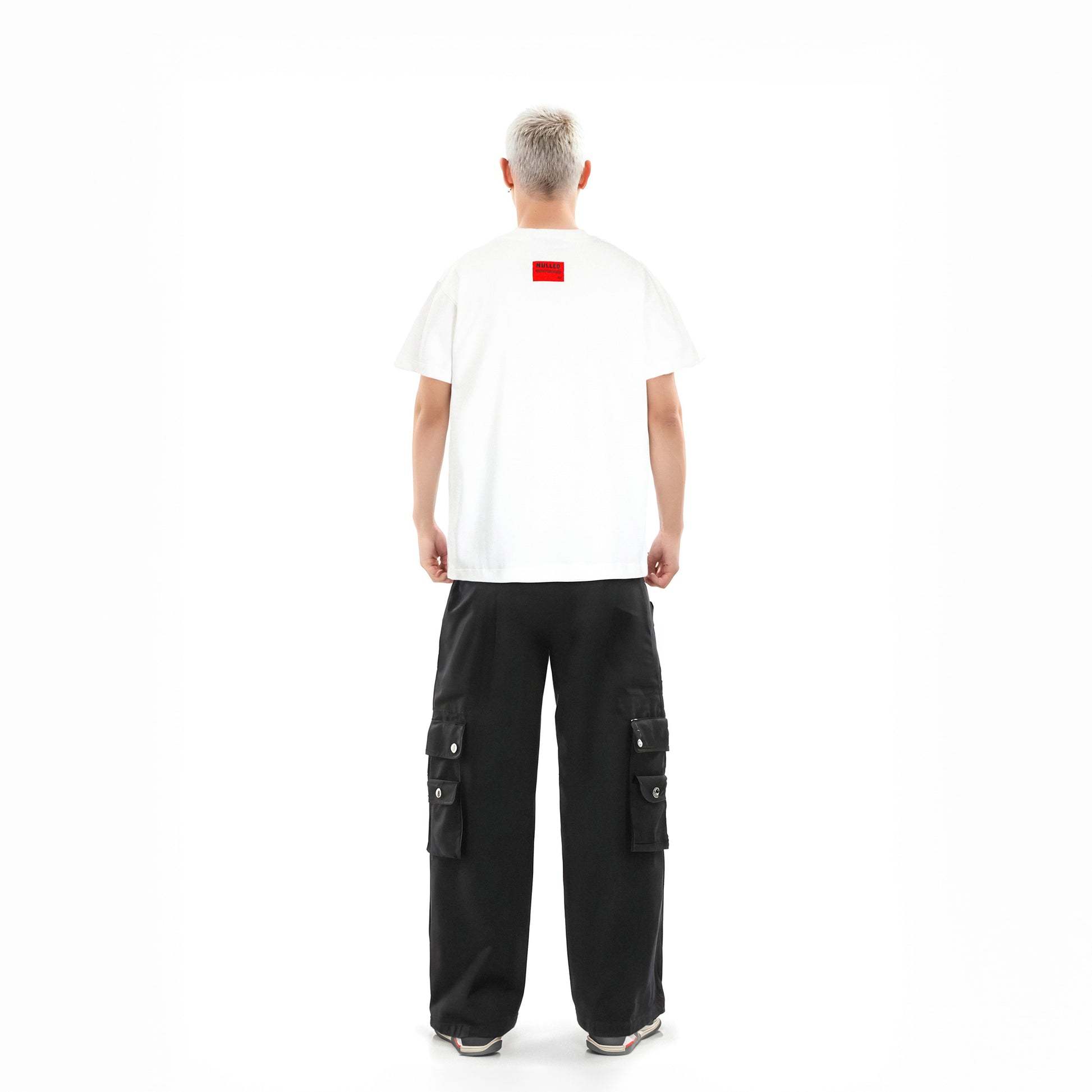 Person wearing a white t-shirt with a red logo and black cargo pants on a white background