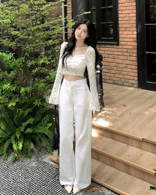 Woman in a white outfit standing on a wooden porch with greenery around.