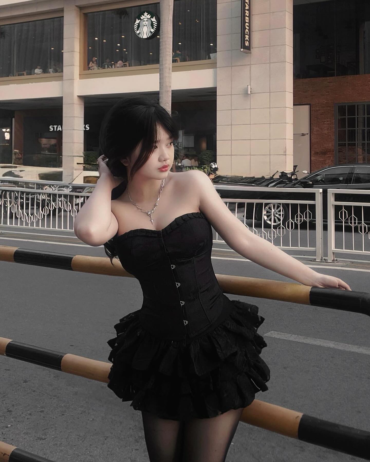 Woman in a black dress standing on a street with a Starbucks building in the background
