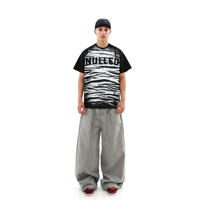 Person wearing a black and white graphic t-shirt with text, gray pants, and red shoes on a white background
