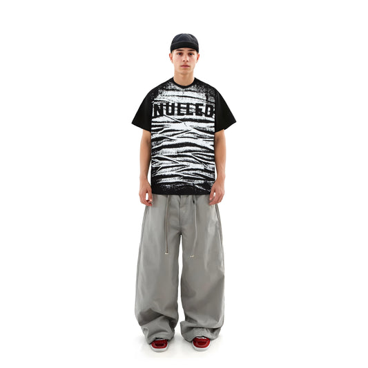 Person wearing a black and white graphic t-shirt with text, gray pants, and red shoes on a white background