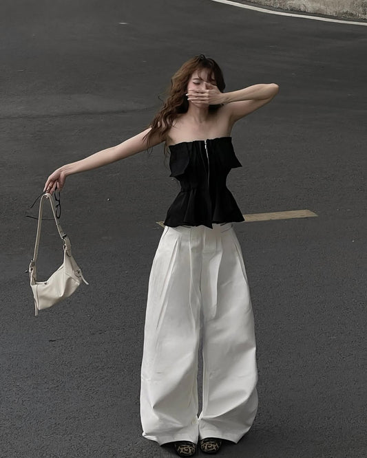 Woman in black top and white pants holding a beige bag on a dark road.