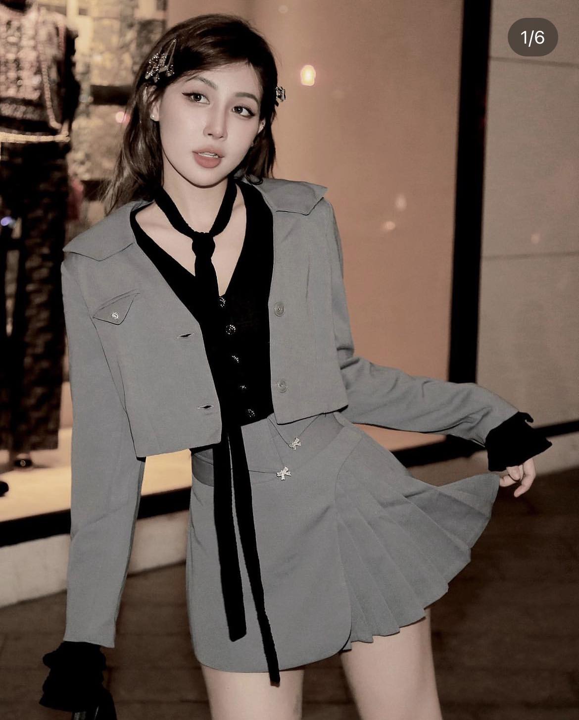 Woman wearing a gray outfit with a black tie and skirt in an indoor setting