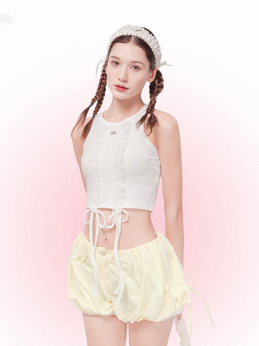 Woman wearing a white sleeveless top and yellow shorts with a pink background