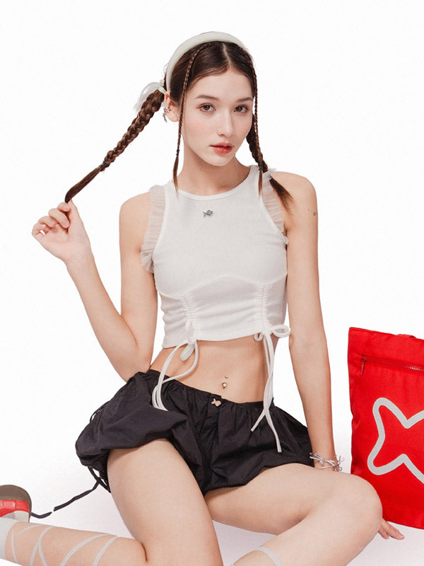 Woman in white crop top and black shorts sitting on a white background with a red bag.