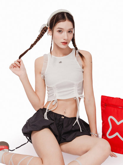 Woman in white crop top and black shorts sitting on a white background with a red bag.