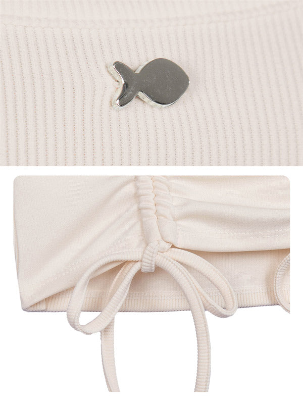 Close-up of a textured beige fabric with a small fish-shaped brooch and a white drawstring bag.