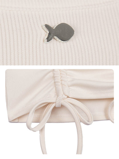 Close-up of a textured beige fabric with a small fish-shaped brooch and a white drawstring bag.