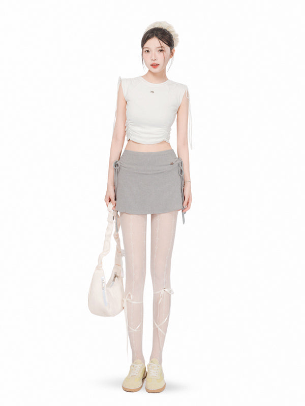 Woman wearing a white sleeveless top and gray skirt with a white bag on a white background