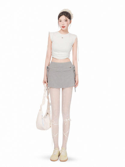 Woman wearing a white sleeveless top and gray skirt with a white bag on a white background