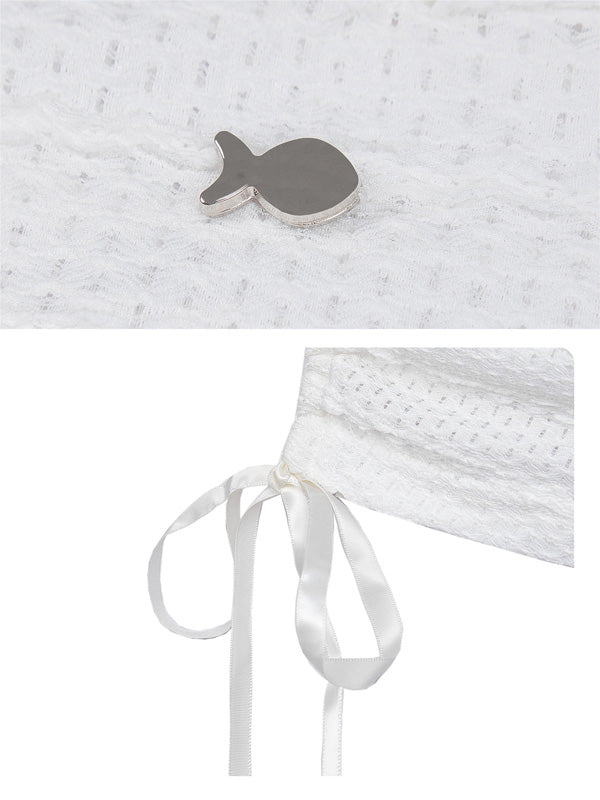 Close-up of a textured white fabric with a fish-shaped object and a white ribbon on a light gray background.