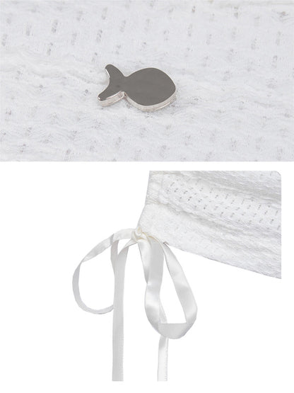 Close-up of a textured white fabric with a fish-shaped object and a white ribbon on a light gray background.