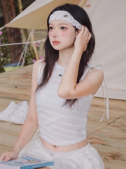 Woman in a light gray sleeveless top and white pants sitting on a wooden floor with a book.