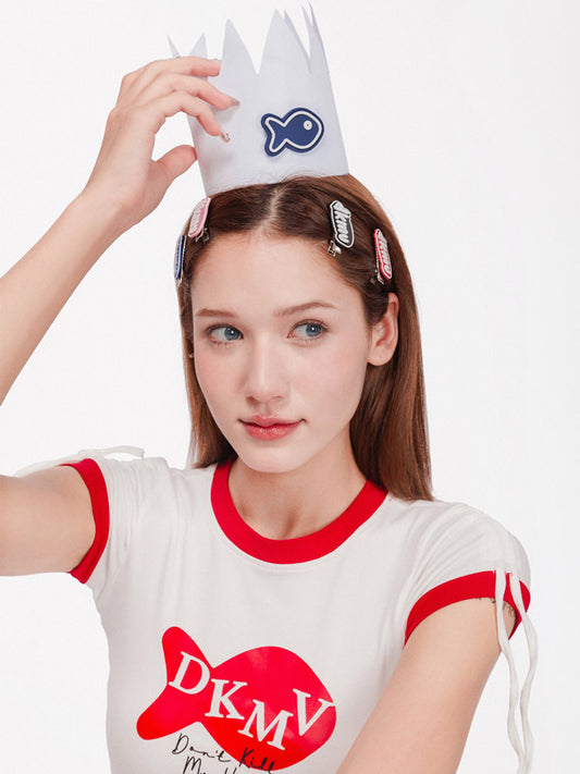 Person wearing a white t-shirt with red accents and a paper crown with a fish design on a white background