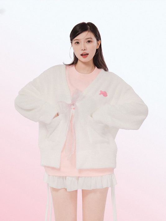 Woman wearing a light-colored cardigan over a pink top on a white background