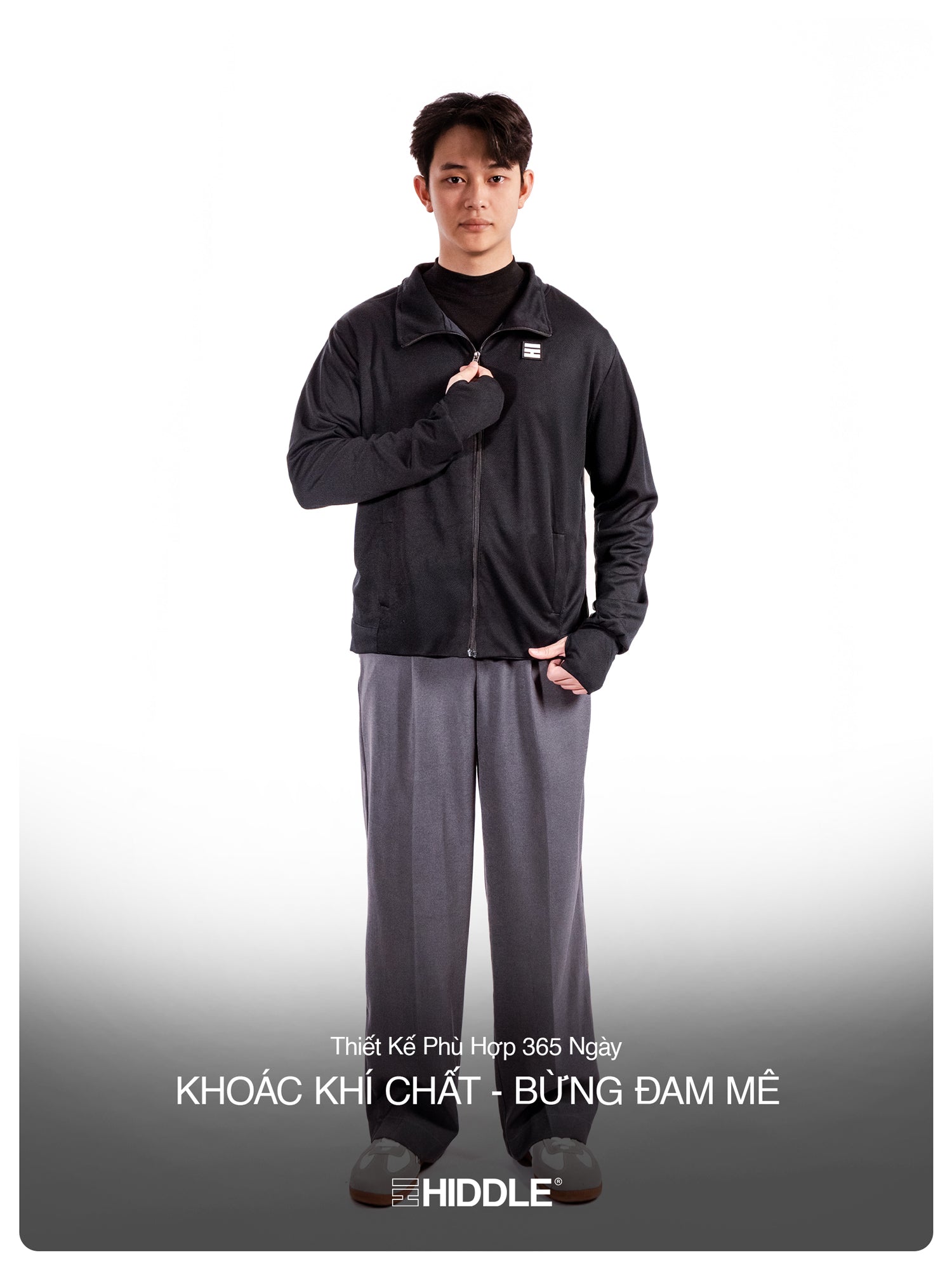 Person wearing a black jacket and gray pants with a visible brand logo on a white background