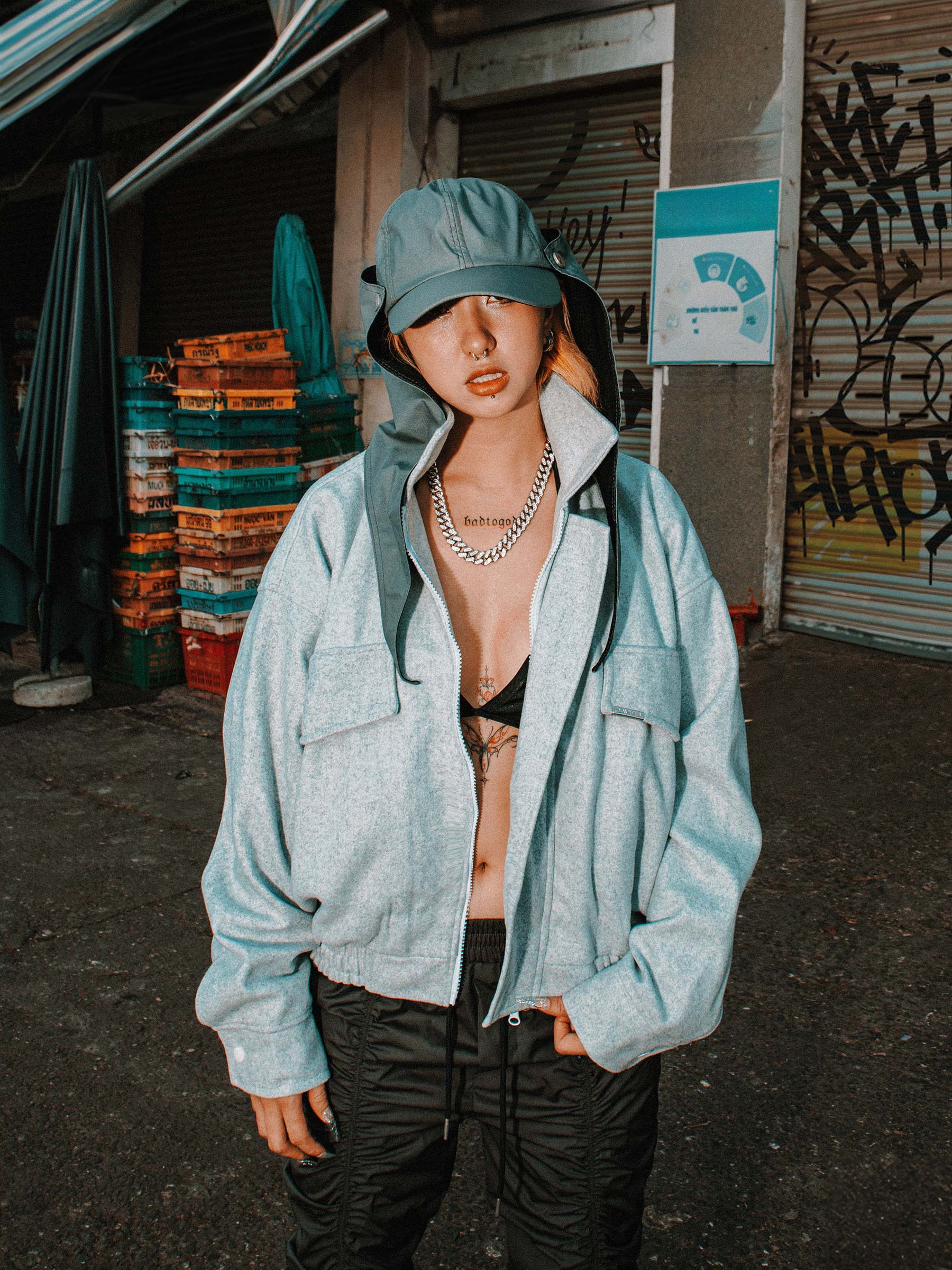 Person wearing a light blue jacket and cap in an urban setting with graffiti on walls.