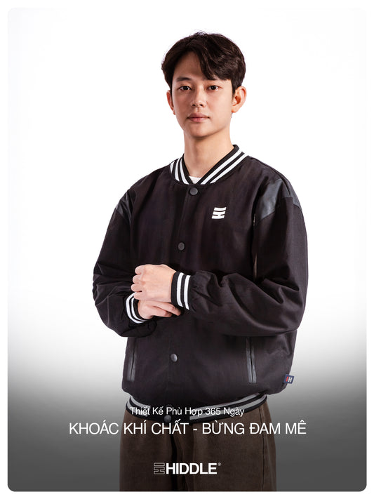 Person wearing a black varsity jacket with white accents on a white background