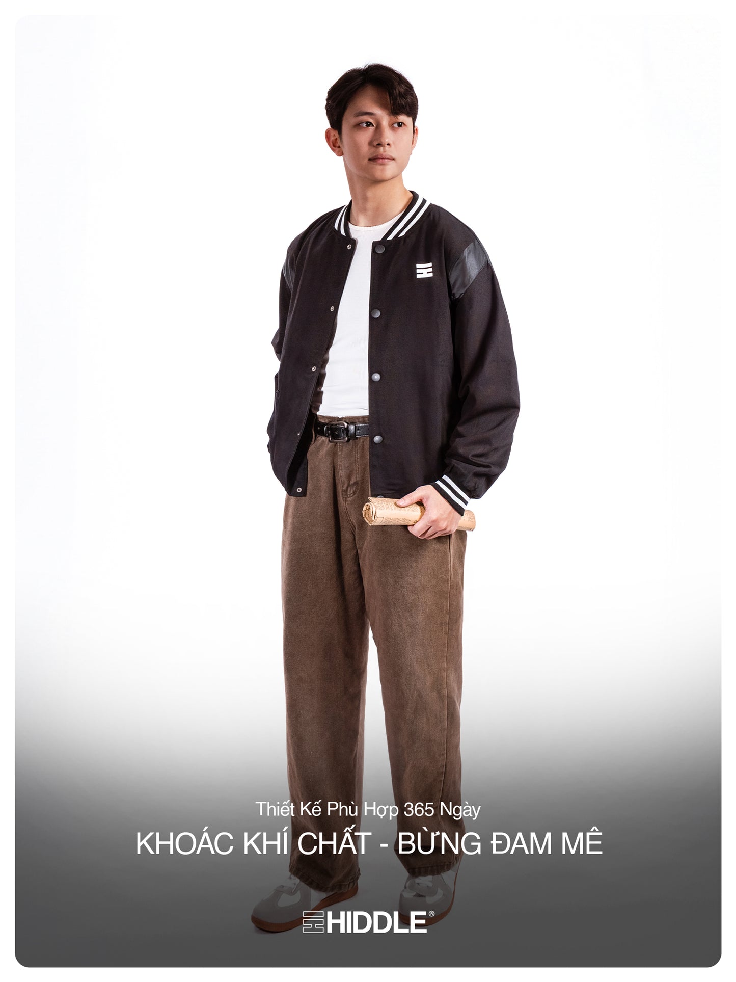 Person wearing a black varsity jacket and brown pants on a white background