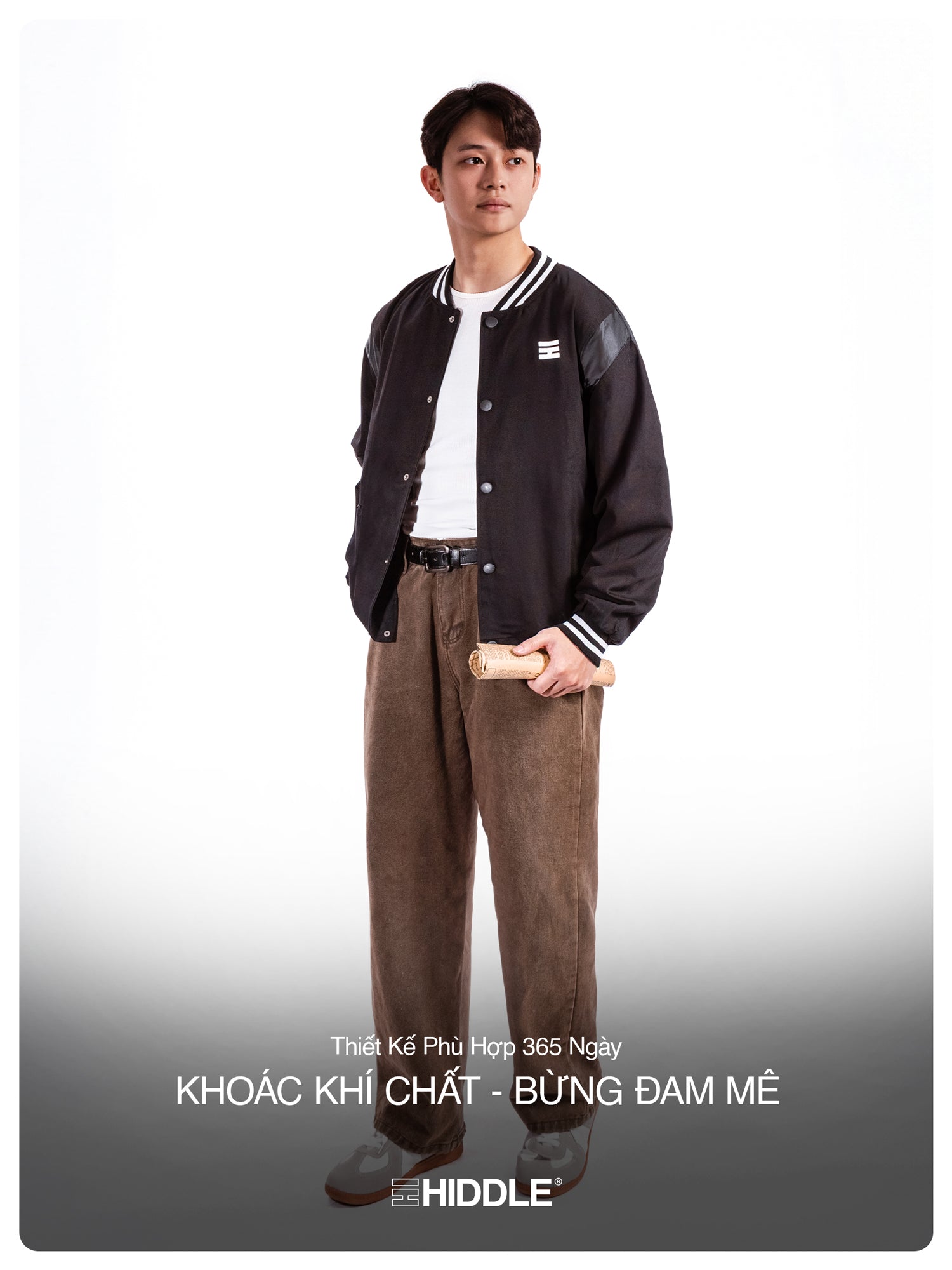 Person wearing a black varsity jacket and brown pants on a white background