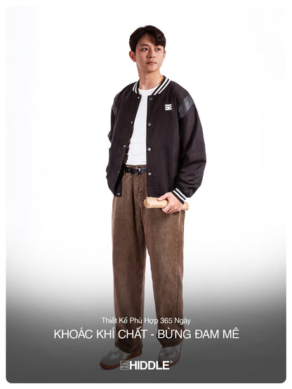 Person wearing a black varsity jacket and brown pants on a white background