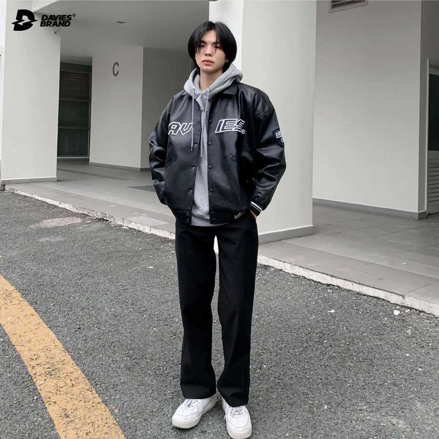 Person wearing a black jacket with logos standing on a street.