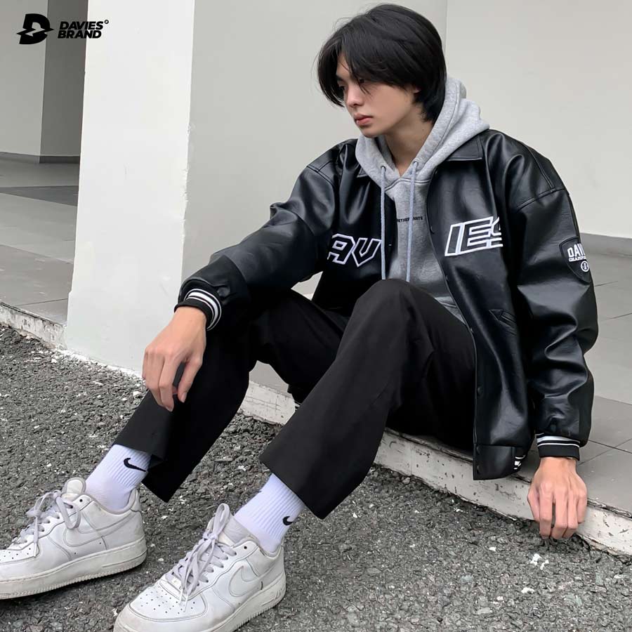 Person wearing a black leather jacket with visible branding, sitting on a concrete floor.