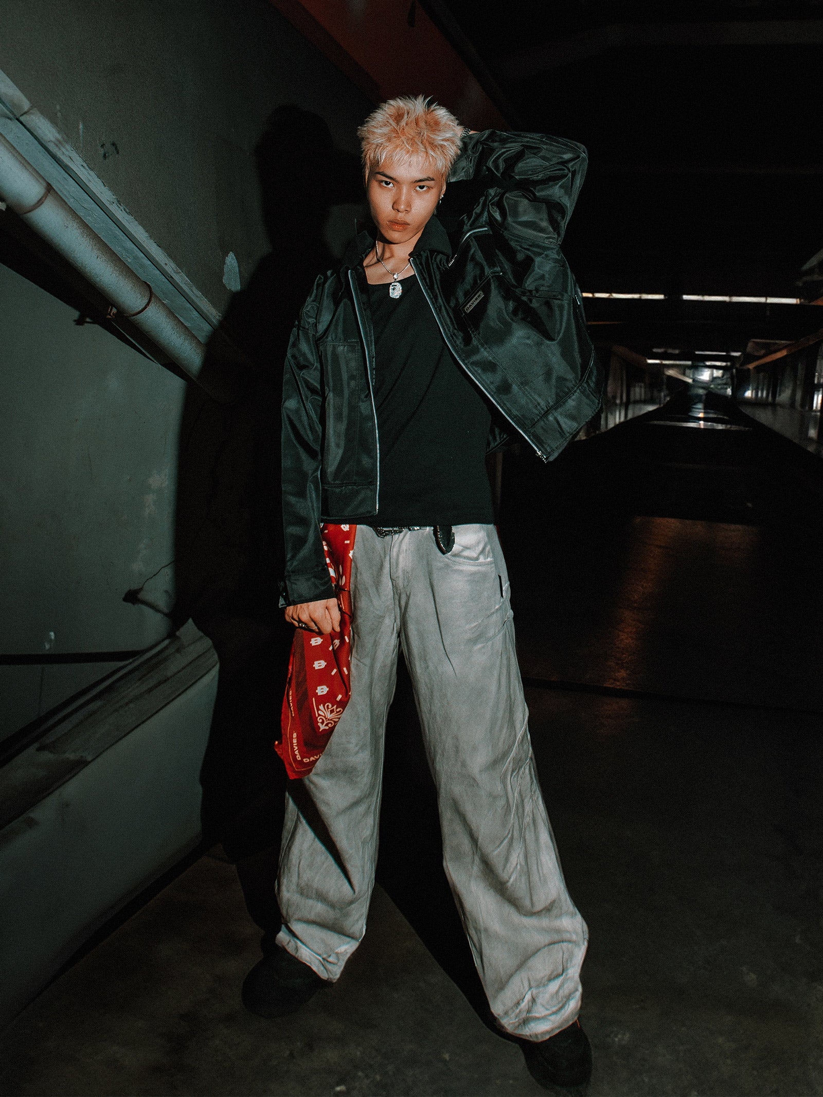 Person wearing a dark green jacket and light gray pants in a dimly lit hallway.