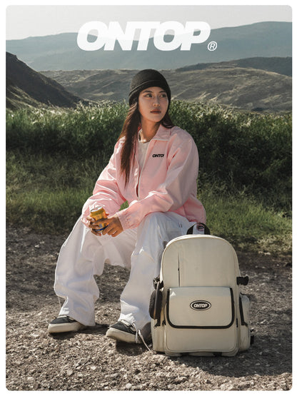 Person sitting outdoors with a backpack, wearing a pink jacket and white pants, with 'ONTOP' branding.