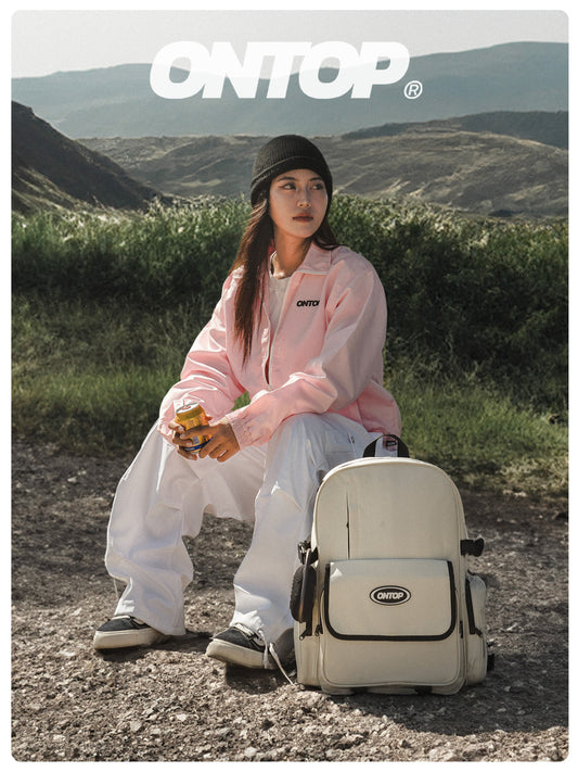 Person sitting outdoors with a backpack, wearing a pink jacket and white pants, with 'ONTOP' branding.