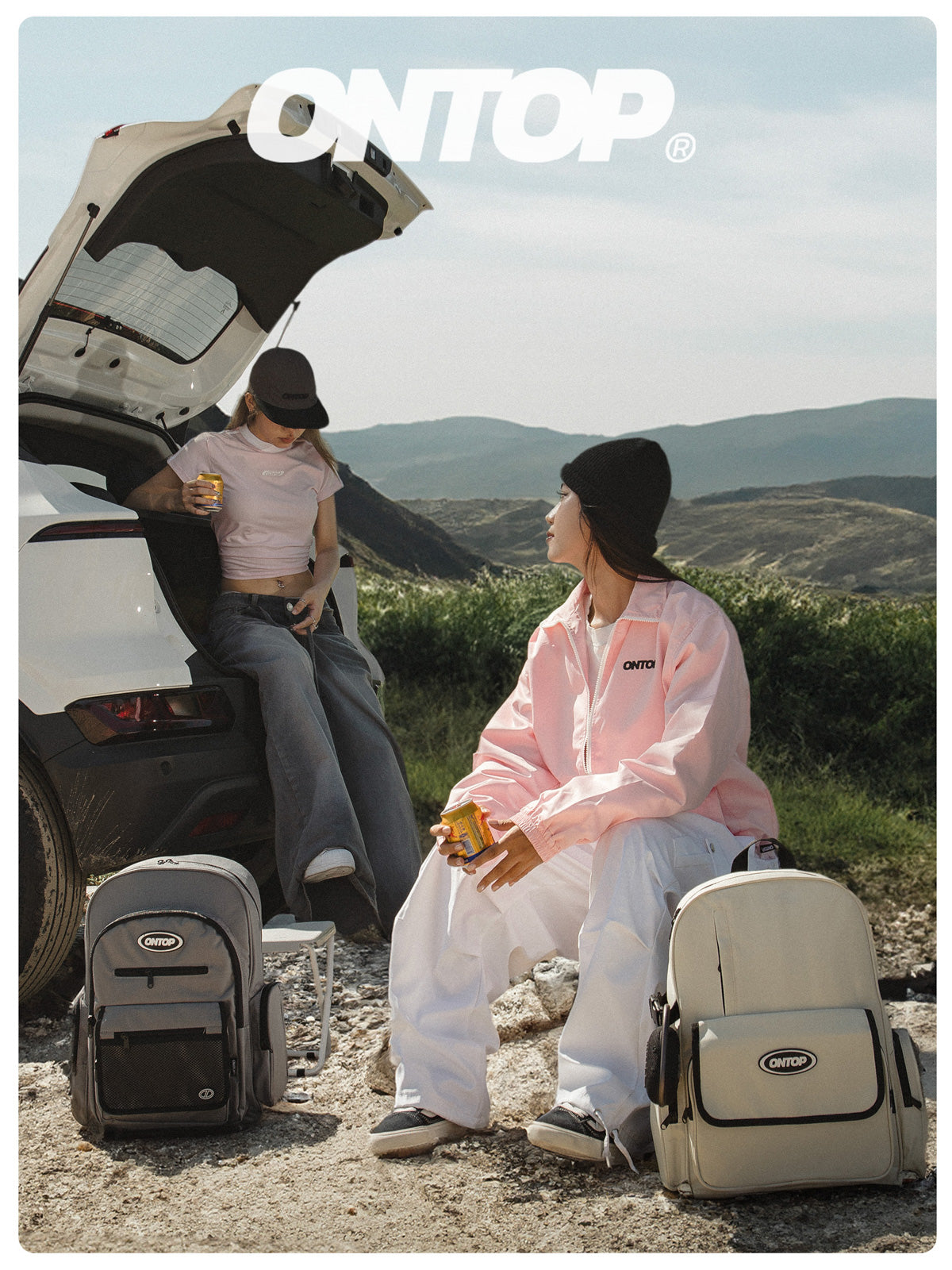 Two people sitting by an open car with ONTOP branded luggage in a scenic outdoor setting.